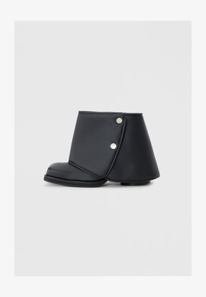 Schwarze Knöchelstiefel aus glattem synthetischen Leder mit einem einzigartigen gefalteten Design, metallischen Druckknöpfen und einer flachen Sohle.