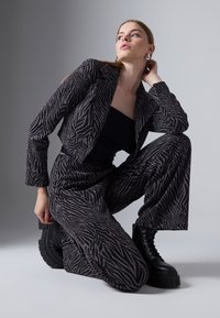 Zwarte en zilveren zebra-print blazer en bijpassende broek, gecombineerd met zwarte platformlaarzen. Gladde textuur, op maat gemaakte pasvorm en onderscheidend patroon.