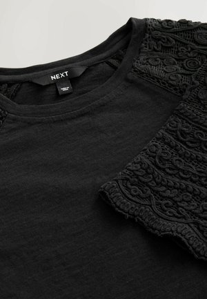 Black t-shirt with a round neckline and textured black embroidered sleeves, made from soft fabric with a smooth finish.