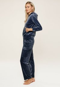 Ensemble de survêtement en velours bleu marine comprenant un hoodie zippé et un pantalon ample avec de grandes poches avant, texture lisse et design simple.