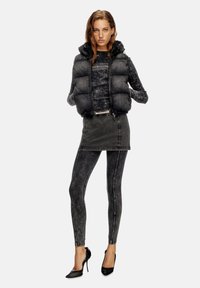 Vestă puffer neagră peste un top negru cu imprimeu tie-dye, asortată cu o fustă mini din denim închis și colanți asortați, completată cu tocuri înalte negre.