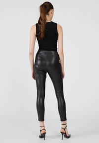 Czarne legginsy z ekoskóry o dopasowanym kroju, z wysokim stanem i gładką fakturą, zestawione z czarnymi wysokimi obcasami na ramiączkach.