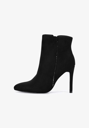 Čierna semišová členková čižma s ostrou špičkou, štíhlym ihličkovým opätkom a bočným zipsom zdobeným kryštálovým detailom pozdĺž okraja.