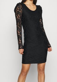 Schwarzes Spitzenkleid mit langen, transparenten Spitzenärmeln und einer taillierten Silhouette. Verfügt über florale Muster und einen Ausschnitt in U-Form.