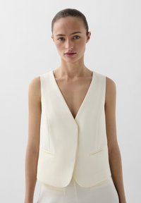 Witte mouwloze vest met een diepe V-hals, textuurstof en twee voorzakken, ontworpen voor een getailleerde look.