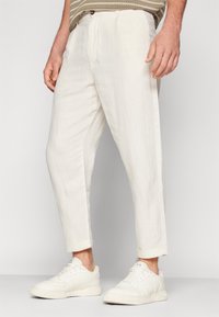 Vita linnebyxor med lös passform, veck, uppkavlade muddar och kombinerade med vita sneakers. Mjuk textur, minimalistisk design.