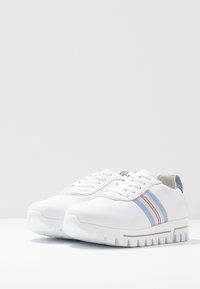 Sneaker bianche con finitura in pelle liscia, caratterizzate da strisce blu e rosa, suola bianca spessa e design tradizionale con lacci.