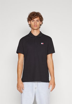 Camisa polo negra de algodón con cuello y mangas cortas. Presenta un pequeño logotipo multicolor en el lado izquierdo del pecho.