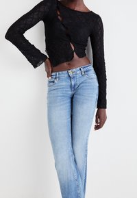 Svart spetsblus med långa ärmar, rundad nederkant och sidokutningar, kombinerad med ljusblå raka jeans med en blekt finish.