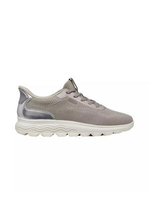 Zapatilla deportiva de color gris claro con parte superior de punto, cierre de cordones, detalle metálico en el talón y suela de goma blanca gruesa y ondulada.