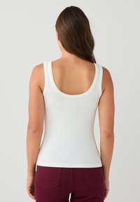 Weißes, geripptes Tanktop mit rundem Ausschnitt hinten, breiten Trägern und taillierter Passform, kombiniert mit burgunderroten Hosen.