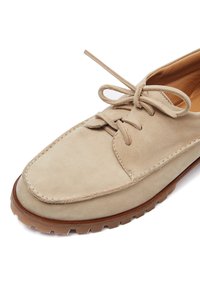 Zapato de ante beige con cordones, puntera redonda, detalles cosidos y suela de goma con un patrón de tracción.
