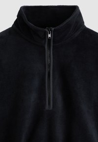 Μαύρο φλις πουλόβερ με ψηλό γιακά και μισό φερμουάρ. Λείο υλικό, ελάχιστες ραφές και διακριτικό αντίθετο τελείωμα κατά μήκο ς του φερμουάρ.