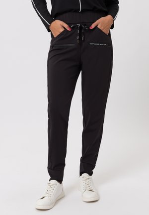 Zwarte sportbroek gemaakt van rekbare stof, voorzien van een elastische tailleband, trekkoord, zakken met ritsen en een bedrukte slogan aan de voorkant.