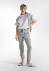 Pantalones deportivos grises con cintura de cordón, combinados con una camiseta blanca de manga corta con letras en relieve, rematados con un cárdigan gris claro.