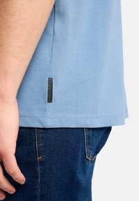 Svetlomodré bavlnené tričko s krátkym rukávom. Na spodnej ľavej strane má malú čiernu štítok. Kombinované s tmavomodrými džínsami.