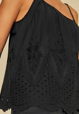 Svart ärmlös topp med intrikat broderi och pärlprydnad. Texturerad skaldel med diamantformade utskärningar för extra detalj.