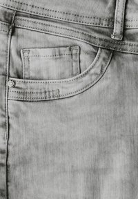 Harmaa denim-kangas, jossa on taskupaneeli, koristetikkaukset ja metallinappi. Pintakuvio on sileä ja siinä on heikko twill-kuvio.