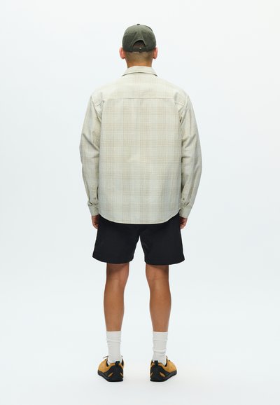 Chemise à manches longues à carreaux beige et vert, associée à un short noir. Dotée d'une coupe décontractée, de poignets à boutons et d'un ourlet arrondi.