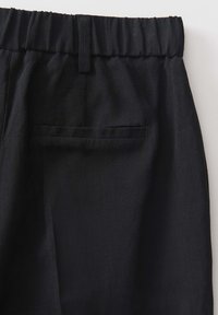 Black linen trousers with an elastic waistband, featuring a single welt pocket at the back and a textured fabric.