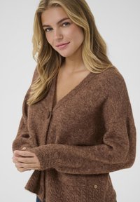 Brązowy sweter cardigan z głębokim dekoltem w kształcie V i pojedynczym zapięciem na guzik. Posiada długie rękawy, ściągacze oraz teksturalne detale.