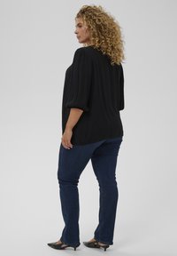 Sort bluse med puffede ærmer, tekstureret stof og en afslappet pasform, kombineret med mørkeblå jeans og sorte spidse sko.