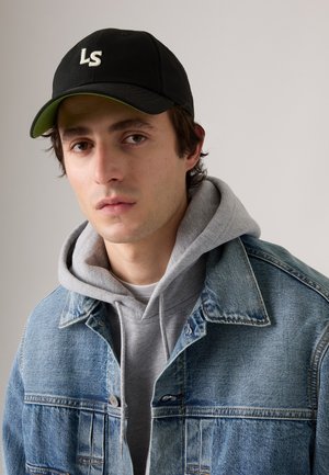 Veste en denim avec délavage bleu clair, sweat à capuche gris superposé en dessous, et casquette noire avec logo blanc. Elle présente un col classique et des boutons à l'avant.