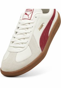 Baskets en cuir blanc avec des accents en suede rouge, comprenant des lacets plats, une languette rembourrée, des détails de logo dorés et une semelle en gomme texturée.