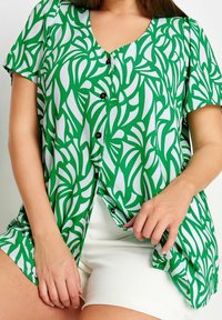 Green and white button-up top featuring a leaf pattern, short sleeves, and a V-neckline. Paired with white shorts.