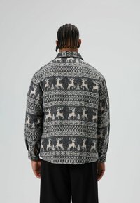 Veste en laine mélangée texturée gris avec un motif blanc de rennes et d'arbres. Design à col, coupe ample et manches avec poignets boutonnés.