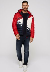 Rød, marineblå og hvid puffjakke med geometrisk design, lynlås-lukning og hætte. Matchende med mørke jeans og hvide sneakers.