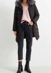 Svart pufferjacka med avtagbar grå pälsluva, i kombination med en ljusrosa ribbad tröja och högmidjade svarta jeans. Svarta klackstövlar.