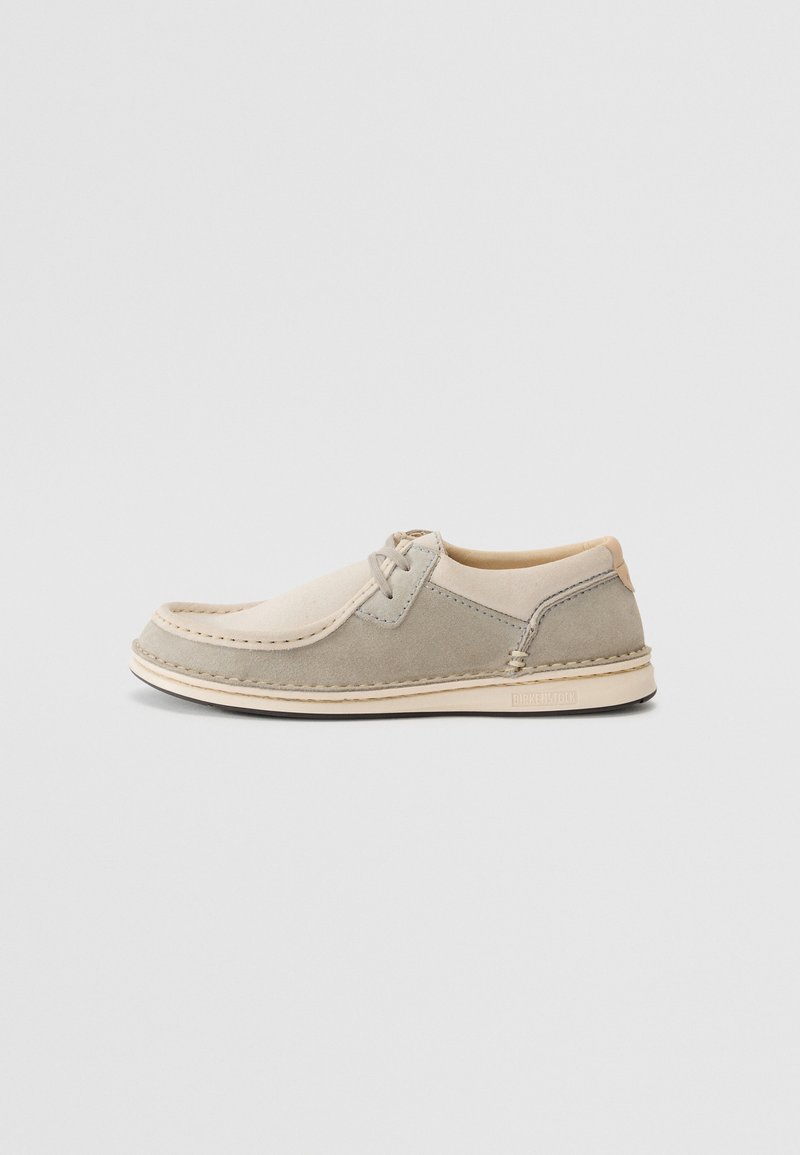 Gray and beige suede slip-on shoe with stitched detailing, round toe, and a contrasting light sole. Brand logo visible on the heel.