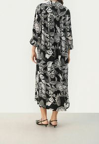 Vestido de media longitud con estampado floral en blanco y negro, mangas de tres cuartos y una silueta fluida. Tejido suave con un corte relajado.