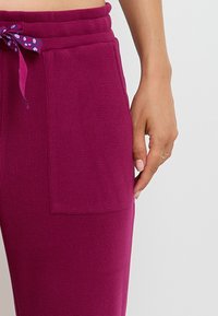 Un pantalon de jogging fuchsia en tissu texturé avec une taille élastique à cordon de serrage et un motif à pois, comprenant des poches latérales pour plus de fonctionnalité.