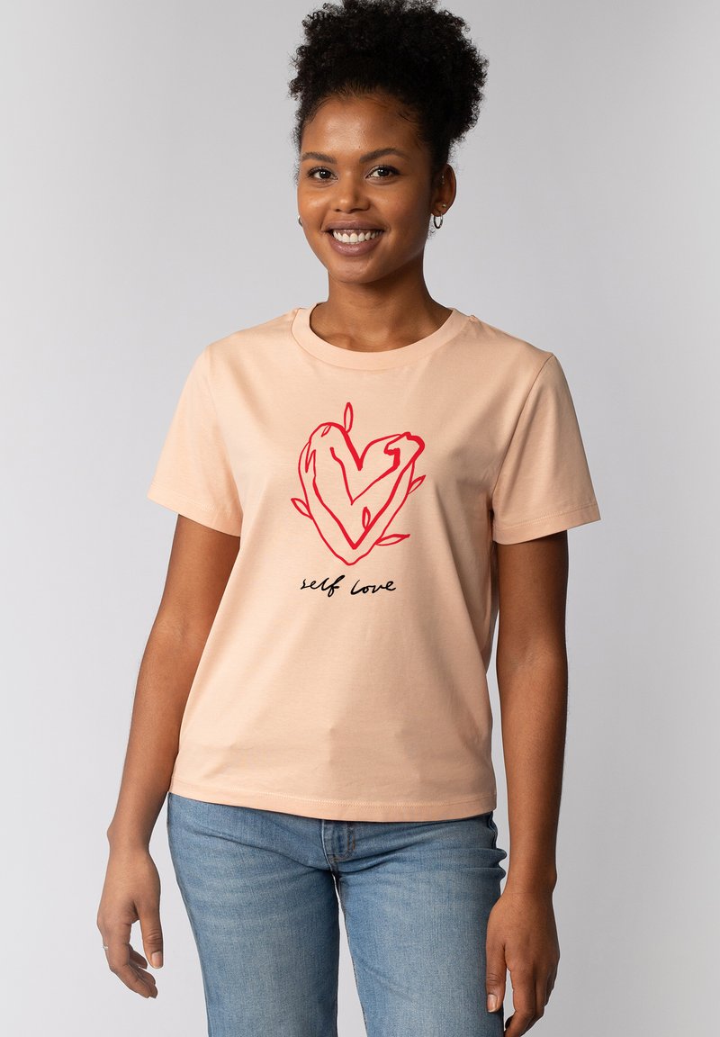 Perzikkleurige t-shirt met korte mouwen, voorzien van een rood hartontwerp en zwarte tekst "self love". Zachte stof, ronde hals, reguliere pasvorm.