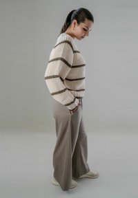 Crème kleurige gebreide trui met donkerbruine strepen, gecombineerd met losse grijze broeken en witte sneakers. Schoon, minimalistisch ontwerp.