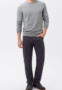 Pull en tricot gris à manches longues, associé à un pantalon gris foncé et des bottines grises. Textures lisses et design simple.