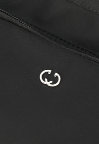 Tessuto in fibra nera con un logo doppio-G argentato visibile. La superficie appare liscia con un bordo cucito e un dettaglio con zip.