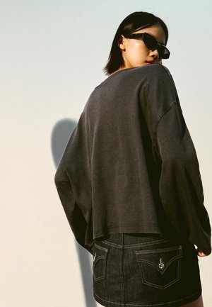 Dark grey oversized sweatshirt with dropped shoulders, paired with a black denim skirt featuring yellow stitching and back pockets.