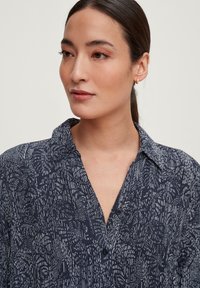 Camicia button-up di colore blu navy con un motivo astratto bianco. Presenta un colletto, una scollatura a V e una vestibilità rilassata. Tessuto dalla texture liscia.