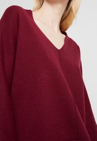 Bourgogne sweater lavet af blødt strikket stof, med V-udskæring, brede ærmer og en søm ned foran.