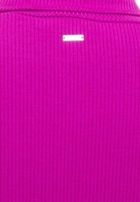 Tessuto a costine di un vibrante color fucsia con una superficie liscia; presenta un'etichetta bianca con due fori sul retro.