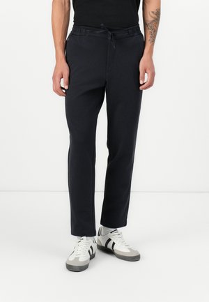 Marineblauwe joggers met een elastische tailleband en trekkoord. Glad weefsel, taps toelopende pijpen en zijzakken. Combinatie met witte sneakers.