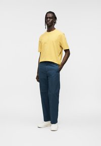 Κίτρινο κοντομάνικο μπλουζάκι σε συνδυασμό με σκούρο μπλε παντελόνι. Το μοντέλο φοράει λευκά αθλητικά παπούτσια. Απλό και μοντέρνο σχέδιο με άνετη εφαρμογή.