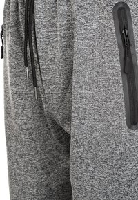 Grå sweatpants med texturerad tyg, elastisk midja, justerbar dragsko och en ficka med dragkedja på sidan med svarta detaljer.