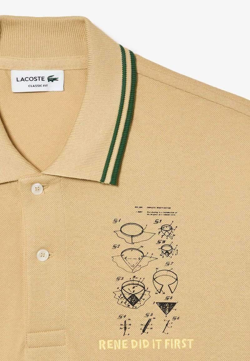 Camisa polo beige con cuello a rayas verdes, que presenta un gráfico impreso de dibujos y el texto "RENE LO HIZO PRIMERO" en amarillo en la parte inferior.