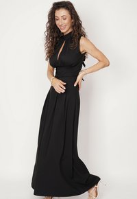 Czarna maxi sukienka z dopasowanym gorsetem, dekoltem w kształcie dziurki oraz kokardą z tyłu. Luźna spódnica z plisami i gładką teksturą materiału.
