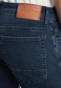 Donkerblauwe denim jeans met een leren label met "Marc O'Polo EST. IN STOCKHOLM" op de tailleband. Gedetailleerde stiksels en klassieke zakken.