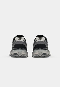 Chaussures de sport noires et grises avec une tige texturée, des panneaux en mesh et une semelle ondulée et rembourrée avec un accent brillant.